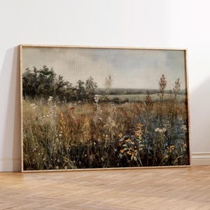 Puede incluir: Una pintura enmarcada que representa un campo de flores silvestres en tonos de azul, morado, amarillo y naranja. El campo se encuentra en un fondo de bosque lejano y cielo nublado.