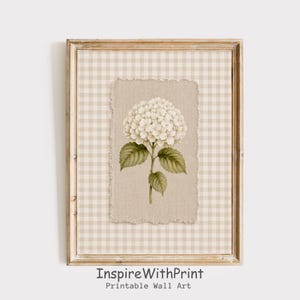 Könnte beinhalten: Gerahmtes Wandbild mit einer Aquarellillustration einer weißen Hortensienblüte mit grünen Blättern. Das Kunstwerk ist vor einem beigefarbenen Hintergrund mit Vichy-Karo-Muster und einem zerrissenen Papiereffekt platziert. Der Rahmen ist hellbraun. Der Text "InspireWithPrint Printable Wall Art" steht unten.