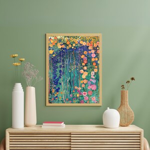 May include: A framed painting of a colorful floral garden with a variety of flowers in shades of pink, yellow, blue, and green. The painting is set against a green wall with two vases and a stack of books on a wooden shelf.