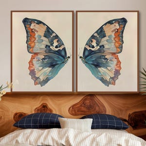 May include: Two framed prints of a watercolor butterfly wing with blue, orange, and white colors. The wings are mirrored images of each other.