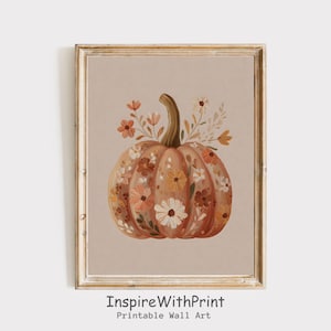 May include: A framed print of a pumpkin adorned with orange, peach, and white flowers. The pumpkin has a brown stem and is set against a neutral background. The text "InspireWithPrint Printable Wall Art" is at the bottom of the print.