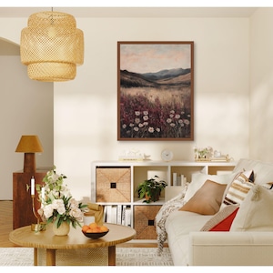 Pode incluir: Uma pintura de paisagem emoldurada que retrata um campo de flores silvestres com uma cordilheira de montanhas ao fundo. A pintura est&aacute; em uma moldura marrom e est&aacute; pendurada em uma parede branca. A pintura est&aacute; em um ambiente de sala de estar com um sof&aacute;, uma mesa de caf&eacute; e outros itens decorativos.