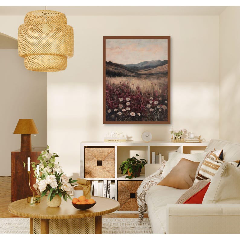 Pode incluir: Uma pintura de paisagem emoldurada que retrata um campo de flores silvestres com uma cordilheira de montanhas ao fundo. A pintura est&aacute; em uma moldura marrom e est&aacute; pendurada em uma parede branca. A pintura est&aacute; em um ambiente de sala de estar com um sof&aacute;, uma mesa de caf&eacute; e outros itens decorativos.