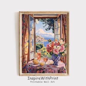 Puede incluir: Impresión enmarcada de una escena escénica a través de una ventana abierta. Una mesa con un mantel floral tiene un jarrón de flores, dos vasos de bebida rosa y limones. La ventana revela un pueblo costero y el mar azul.