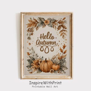 May include: A framed watercolor print with a beige background. The artwork features a wreath of autumn leaves and flowers surrounding the words "Hello Autumn." Two pumpkins and additional flowers are at the bottom. The frame is a light brown color.