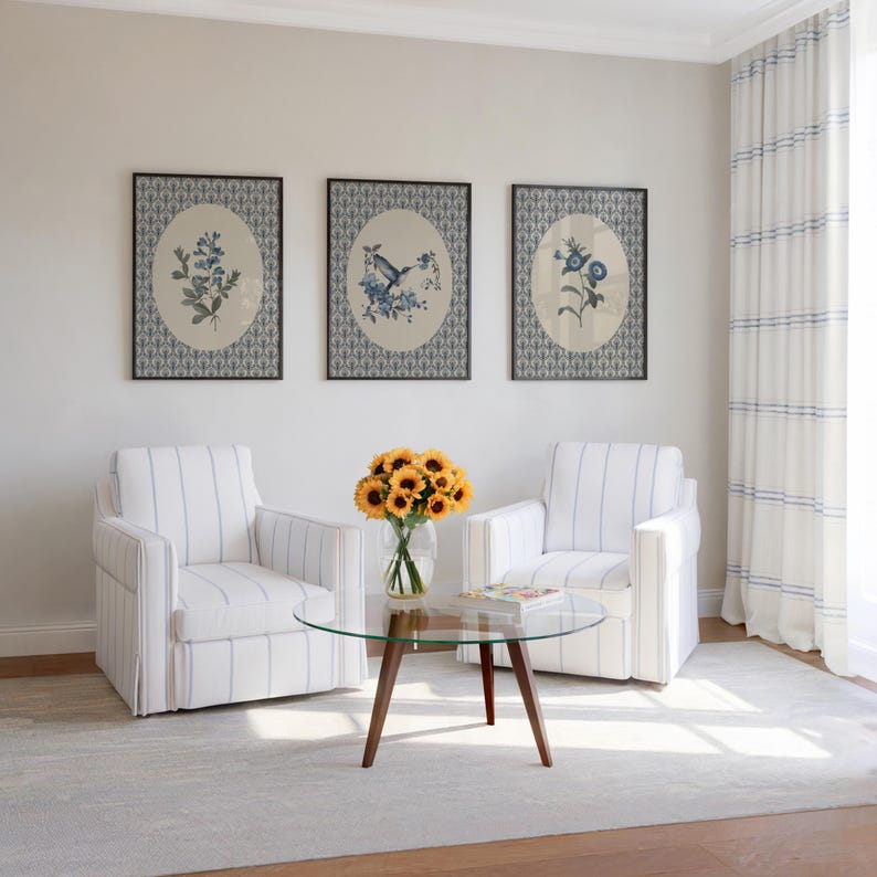 May include: A living room scene featuring two white armchairs with blue striped patterns, a glass-topped coffee table, and three framed botanical prints. A vase of sunflowers sits on the table. The room has a neutral color palette.