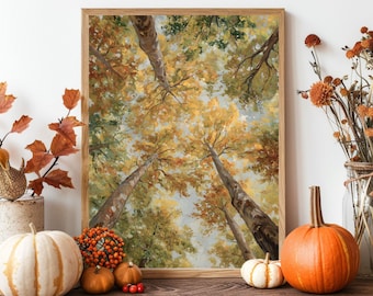 May include: A framed artwork depicts a view looking up through tall trees with yellow and green leaves. Pumpkins, gourds, and fall foliage are arranged in front of the artwork, creating a seasonal display.