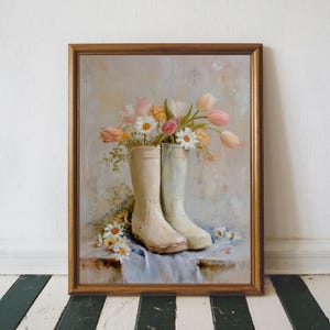 Könnte beinhalten: Gerahmtes Gemälde, das ein Paar cremefarbene Gummistiefel zeigt, gefüllt mit einem Strauß bunter Blumen, darunter rosa und weiße Tulpen und Gänseblümchen. Die Stiefel stehen auf einem blauen Tuch, mit weiteren Blumen verstreut.