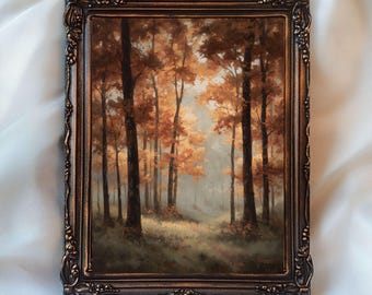 May include: A framed landscape painting of a forest in autumn. The artwork features tall trees with orange and brown leaves, set against a misty background. The ornate, dark bronze frame adds a vintage touch. The text "InspireWithPrint Printable Wall Art" is at the bottom.