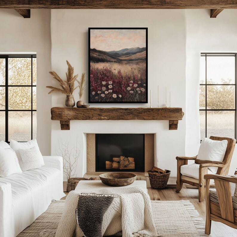 Pode incluir: Uma pintura de paisagem emoldurada que representa um campo de flores silvestres com uma cordilheira de montanhas ao fundo. A pintura est&aacute; em um ambiente de sala de estar r&uacute;stico com uma lareira e um sof&aacute;.