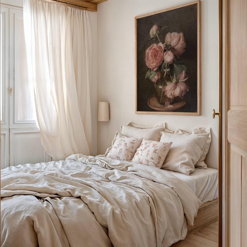 K&ouml;nnte beinhalten: Ein beigefarbener Leinen-Bettbezug mit einem wei&szlig;en, durchsichtigen Vorhang im Hintergrund. Das Bett ist mit zwei beigen Leinenkissen und zwei Kissen mit Blumenmuster bezogen. Ein gerahmtes Gem&auml;lde mit rosa Rosen in einer Vase h&auml;ngt an der Wand &uuml;ber dem Bett.