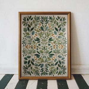 May include: A framed botanical print featuring a symmetrical design of green and blue-green leaves with small yellow flowers. The artwork is set against a cream background and framed in a gold-toned wooden frame. The print is displayed on a black and white striped floor.