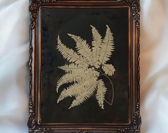 May include: A framed botanical print featuring a detailed fern frond in shades of beige against a dark background. The ornate, bronze-colored frame adds a vintage touch. The text "InspireWithPrint Printable Wall Art" is visible at the bottom.