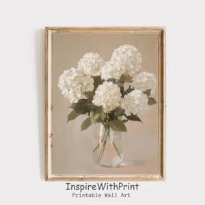 Op de afbeelding: Een ingelijste print met een stilleven van witte hortensia's in een heldere glazen vaas. De bloemen staan centraal, met groene bladeren en stelen. De lijst is lichtgoud van kleur. De tekst "InspireWithPrint Printable Wall Art" staat onderaan.