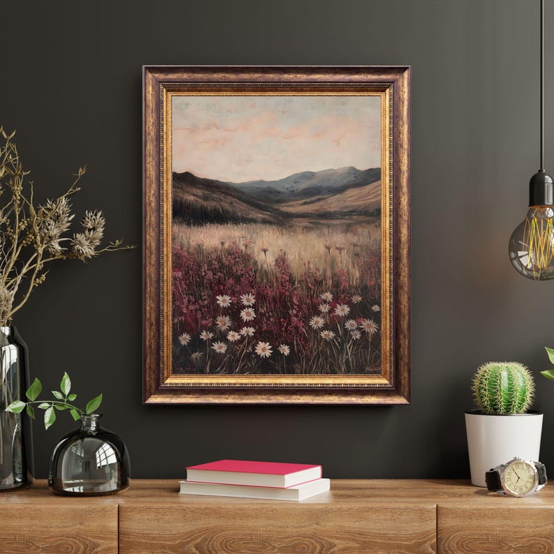 Pode incluir: Uma pintura de paisagem emoldurada que retrata um campo de flores silvestres em um vale com montanhas ao fundo. O c&eacute;u &eacute; de um rosa e azul suaves, e as flores s&atilde;o uma mistura de branco e rosa.