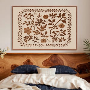 May include: A framed print with a beige background and a brown floral design. The design features a variety of flowers and leaves arranged in a symmetrical pattern. The frame is a simple brown wood frame.