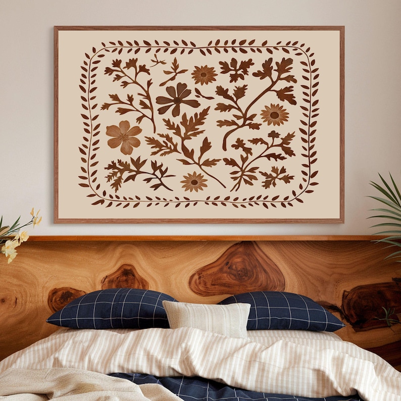 May include: A framed print with a beige background and a brown floral design. The design features a variety of flowers and leaves arranged in a symmetrical pattern. The frame is a simple brown wood frame.
