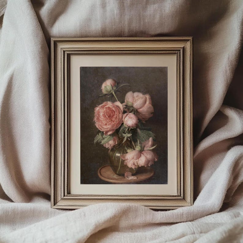 K&ouml;nnte beinhalten: Ein gerahmtes Gem&auml;lde eines Strau&szlig;es rosa Pfingstrosen in einer gr&uuml;nen Vase auf einem braunen Tisch. Das Gem&auml;lde hat einen dunklen Hintergrund und ist in einem hellen Holzrahmen gerahmt.