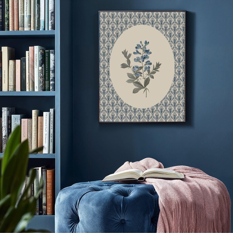 May include: Framed botanical print featuring a blue floral design within an oval shape, set against a cream background. The oval is surrounded by a patterned border in shades of blue and white. The artwork is displayed on a dark blue wall.