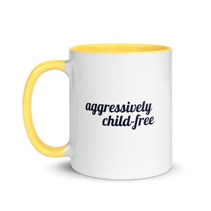 May include: White ceramic mug with a yellow interior and handle. The mug features the text "aggressively child-free" in a dark blue, cursive font. The mug is designed for hot beverages.