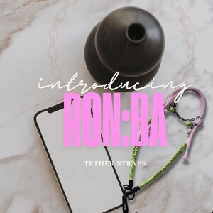 May include: An image featuring a black phone, a black tether strap, and a decorative black object. The text "introducing RON:BA TETHER STRAPS" is displayed in pink and white.