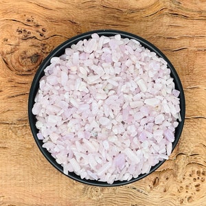 Pode incluir: Uma tigela preta cheia de pequenas lascas de cristal rosa claro e branco.