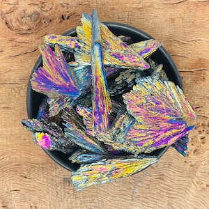 May include: A bowl filled with iridescent, black, purple, and gold crystals. The crystals are arranged in a random pattern and have a metallic sheen.