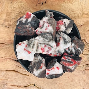 Peut inclure: Une collection de cristaux rouges et noirs dans un bol noir. Les cristaux ont un motif marbré blanc, noir et rouge.