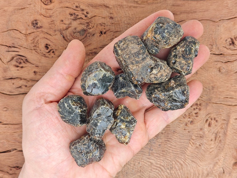 May include: A collection of dark amber stones with a black and brown color variation. The stones are rough and have a natural, unpolished look.