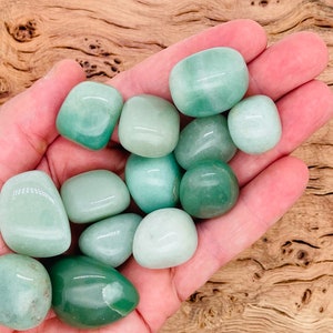 May include: A collection of smooth, green jade tumbled stones in various shades of green. The stones are in a person's hand, showcasing their size and shape.