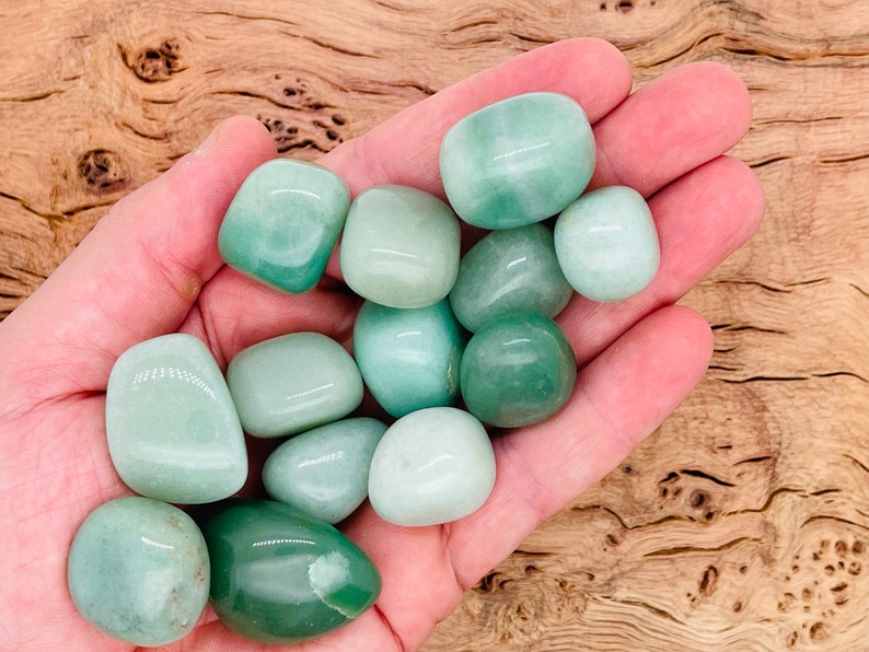 May include: A collection of smooth, green jade tumbled stones in various shades of green. The stones are in a person's hand, showcasing their size and shape.