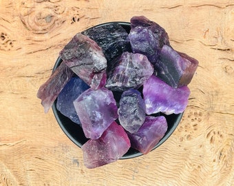May include: A black bowl filled with purple and blue fluorite crystals. The crystals are rough and have a natural, unpolished look.