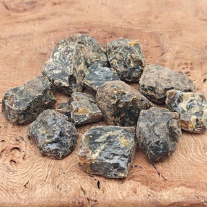 May include: A collection of dark amber stones, with a variety of shapes and sizes, on a wooden surface.