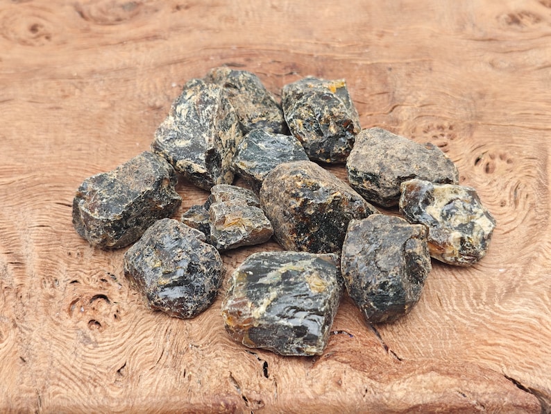 May include: A collection of dark amber stones, with a variety of shapes and sizes, on a wooden surface.
