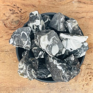 Puede incluir: Un cuenco de piedras pulidas de color negro y blanco. Las piedras tienen un patrón de remolino y son lisas y pulidas.