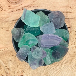 May include: A bowl of green and purple fluorite crystals. The crystals are various sizes and shapes, and they are all tumbled and polished.