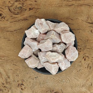 May include: A bowl filled with pink and white tumbled rose quartz stones. The stones are rough and have a natural, unpolished look.