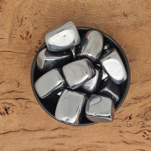 Op de afbeelding: Een kom gevuld met een verzameling gladde, donkergrijze hematiet-tumbled stenen.
