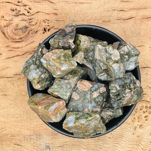 Könnte beinhalten: Eine Schale mit rohen, grünen und blauen Labradorit-Kristallen. Die Kristalle sind eine Mischung aus hell- und dunkelgrün mit blauen Blitzen.