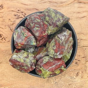 May include: A bowl of red and green aventurine rough stones. The stones are a mix of red, green, and black.