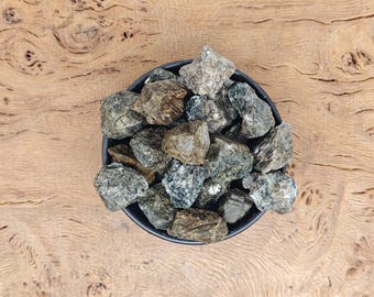 May include: A bowl filled with small, dark green and gray stones. The stones are smooth and have a natural, rough texture.