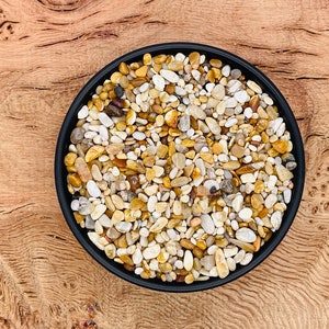 Puede incluir: Un cuenco negro lleno de pequeñas piedras lisas blancas y amarillas. El cuenco está sobre una superficie de madera.