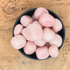 以下が含まれることがあります： 滑らかでピンク色のタンブルストーンが詰まったボウル。石は薄いピンク色で光沢のある仕上がりです。