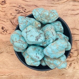 May include: A bowl of turquoise tumbled stones. The stones are a light blue color with brown veins and are smooth and polished.