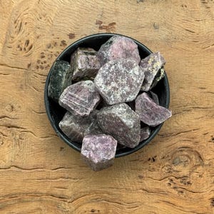 Puede incluir: Un pequeño cuenco lleno de cristales de piedras preciosas en bruto, de color púrpura y gris.