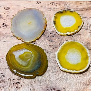 May include: Four agate coasters in various shades of yellow and green. The coasters are round and have a natural, polished finish.