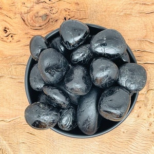 以下が含まれることがあります： 黒いボウルに、黒曜石のタンブルストーンがぎっしり詰まっている。石は滑らかで磨かれており、自然で土のような外観をしています。