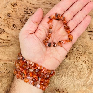 Peut inclure: Un brin de perles de chips de cornaline dans des tons d'orange, rouge et brun. Les perles sont enfilées sur un cordon élastique transparent et mesurent environ 6 mm.