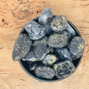 Könnte beinhalten: Eine Schale mit schwarzen und goldenen Trommelsteinen. Die Steine sind glatt und haben verschiedene Formen und Größen.