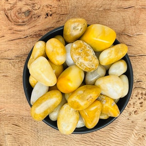May include: A bowl filled with yellow and white tumbled stones. The stones are smooth and polished, and they are arranged in a random pattern.